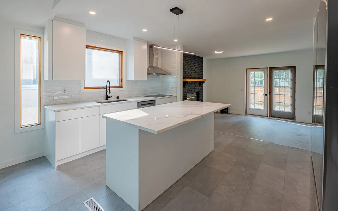 After — the same Winnipeg kitchen opened up: white cabinetry, a quartz waterfall island, subway tile and a re-clad fireplace